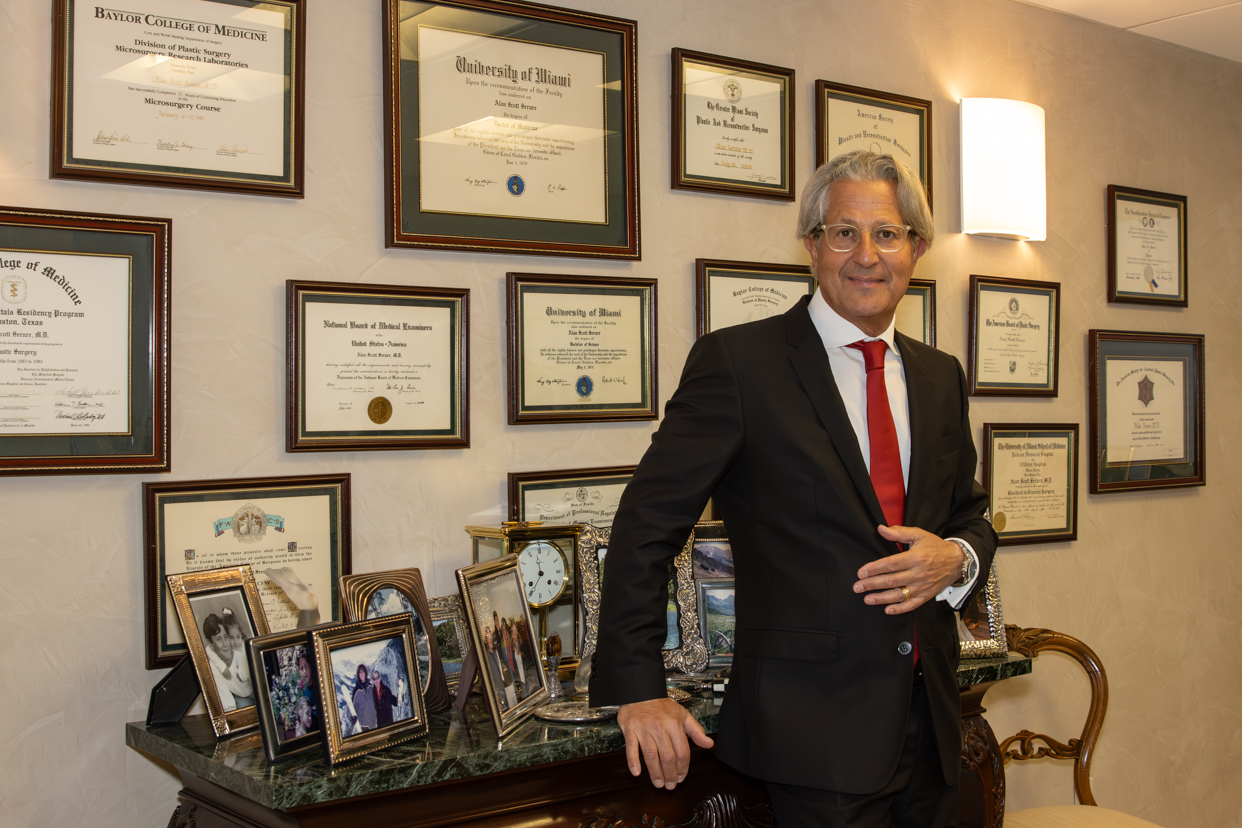 Plastic surgeon, Dr. Alan Serure standing in front of a wall with framed education diplomas and medical certificates.