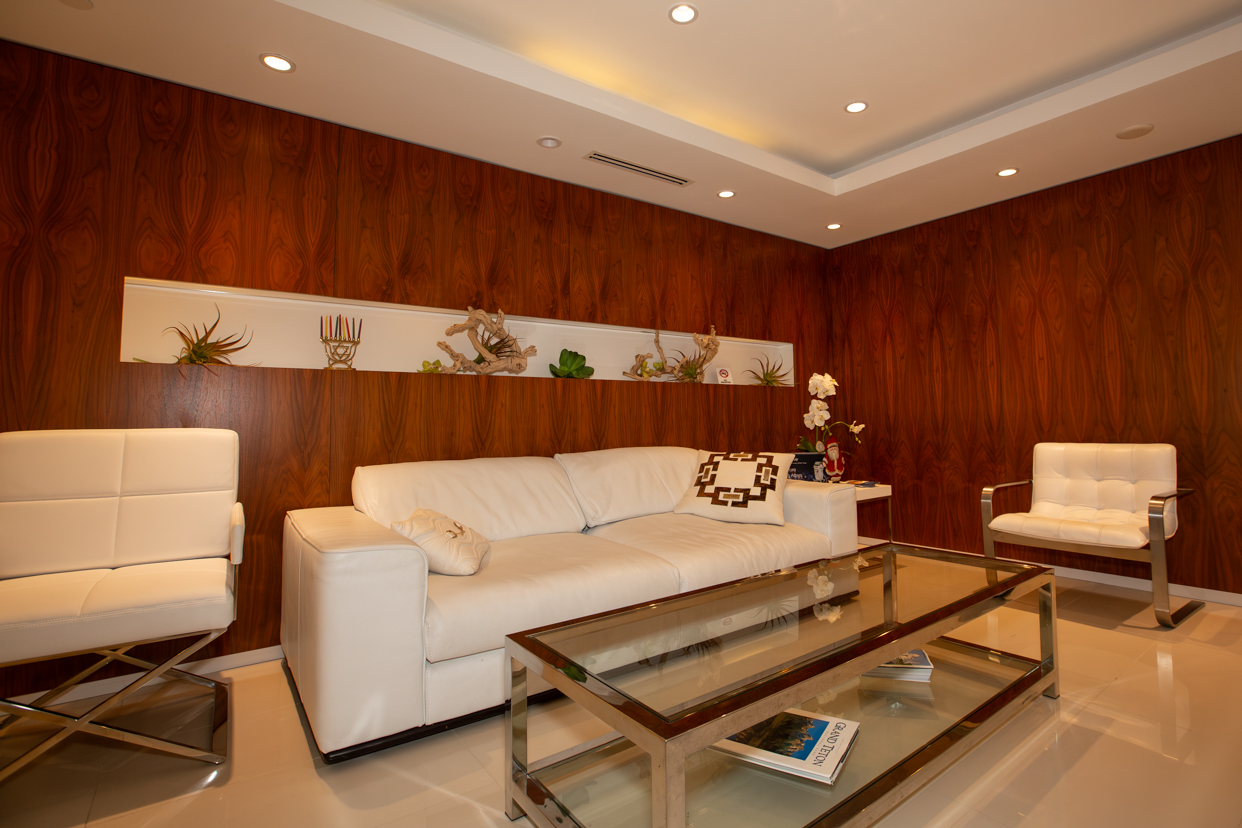 Plastic surgeon, Dr. Alan Serure’s patient sitting area with white sofa and chairs, wood panel walls, and marble floor.