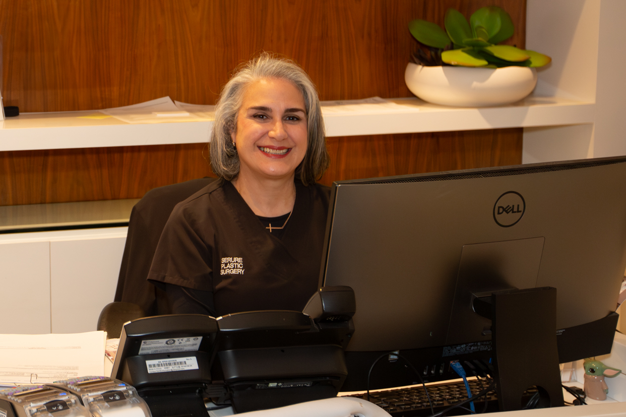 Smiling receptionist sitting at front desk of Dr. Alan Serure’s plastic surgery practice in Miami.